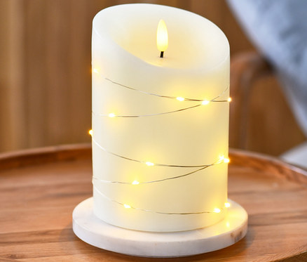 Une bougie à LED en cire véritable avec micro-guirlande lumineuse est posée sur une table ronde en bois.