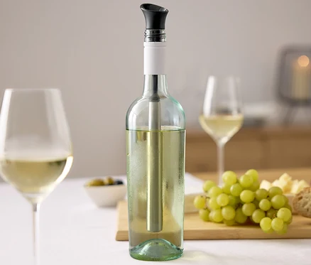 Bouteille de vin avec un bâton réfrigérant pour vin, deux verres de vin, des raisins, du fromage et du pain sur une table.