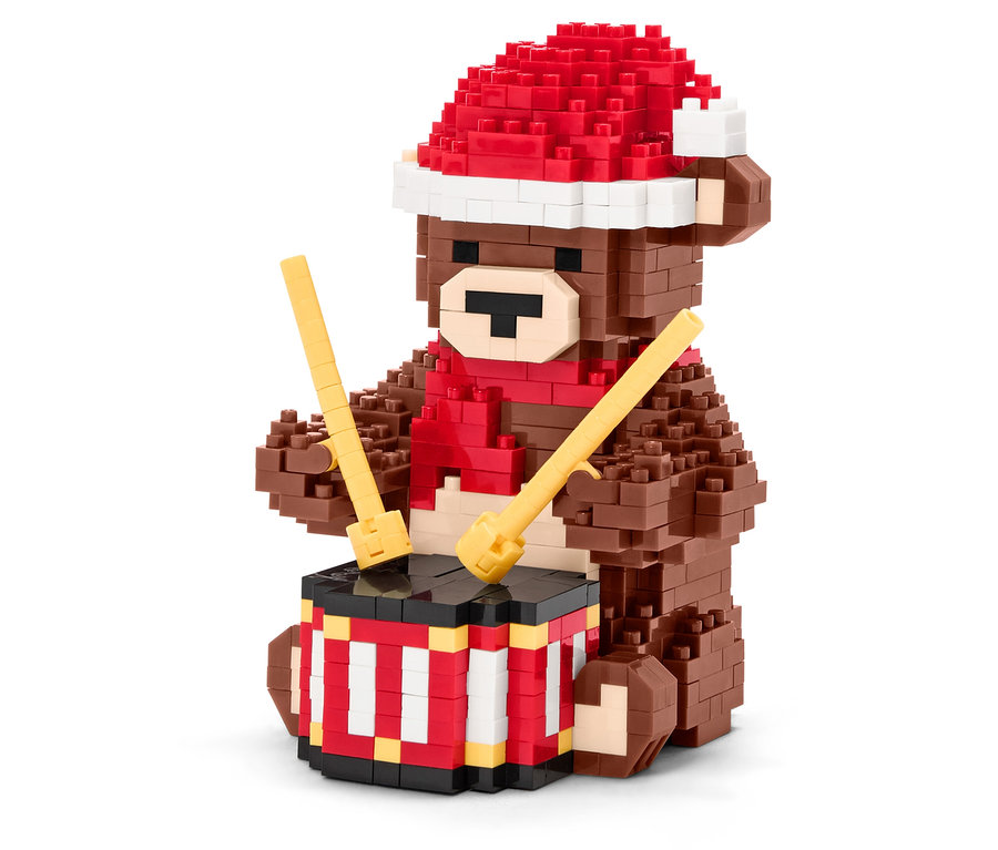 Un ours en briques marron avec un bonnet et une écharpe rouges joue du tambour avec des baguettes.