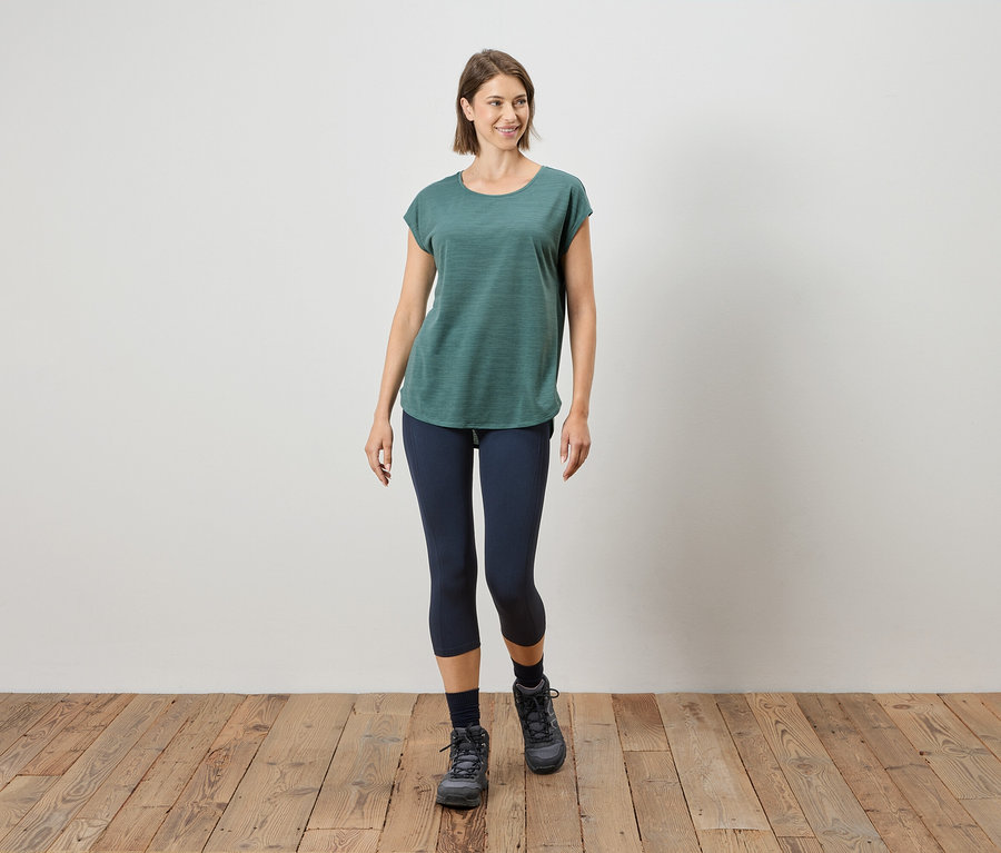 Femme marchant sur un plancher en bois en t-shirt vert, leggings bleus et bottes grises.