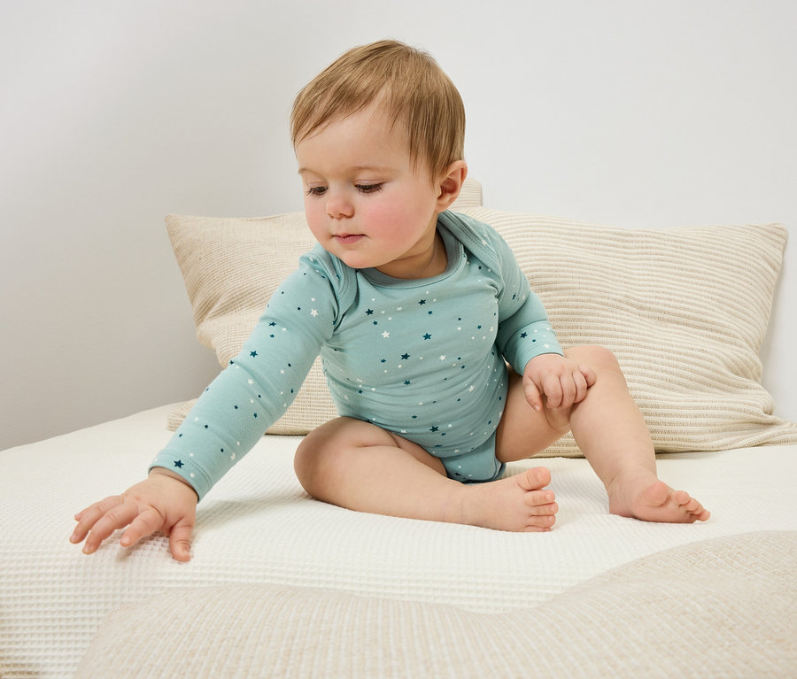 Un bébé est assis sur un lit et tend la main vers une couverture.