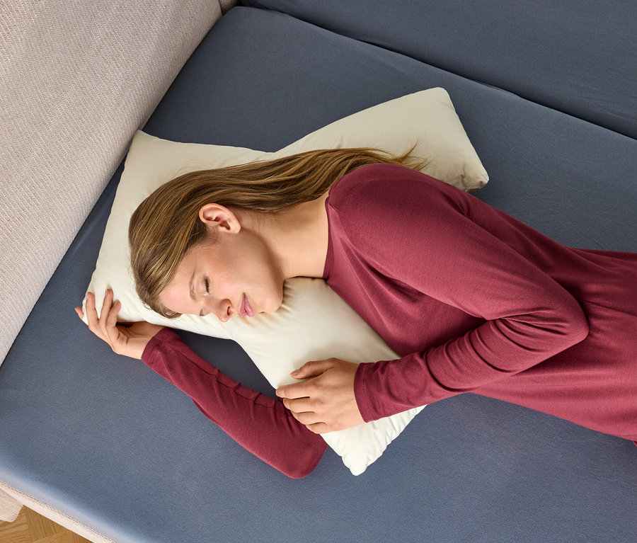 Une femme en chemise de nuit bordeaux dort sur un oreiller blanc sur un lit bleu.
