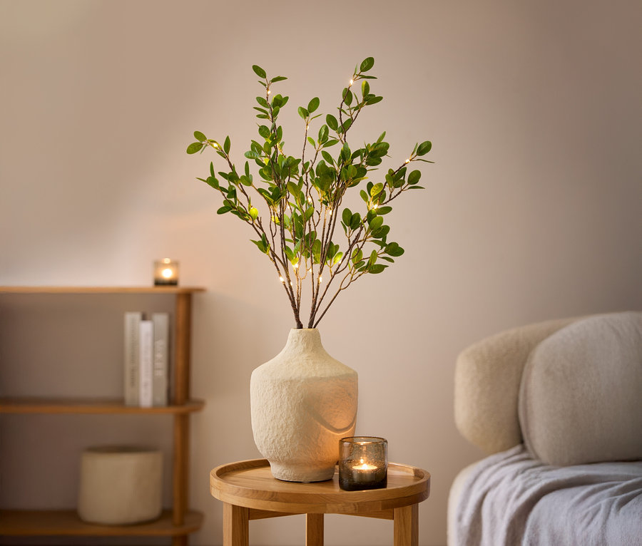 Deux branches décoratives LED dans un vase blanc sur une table en bois.