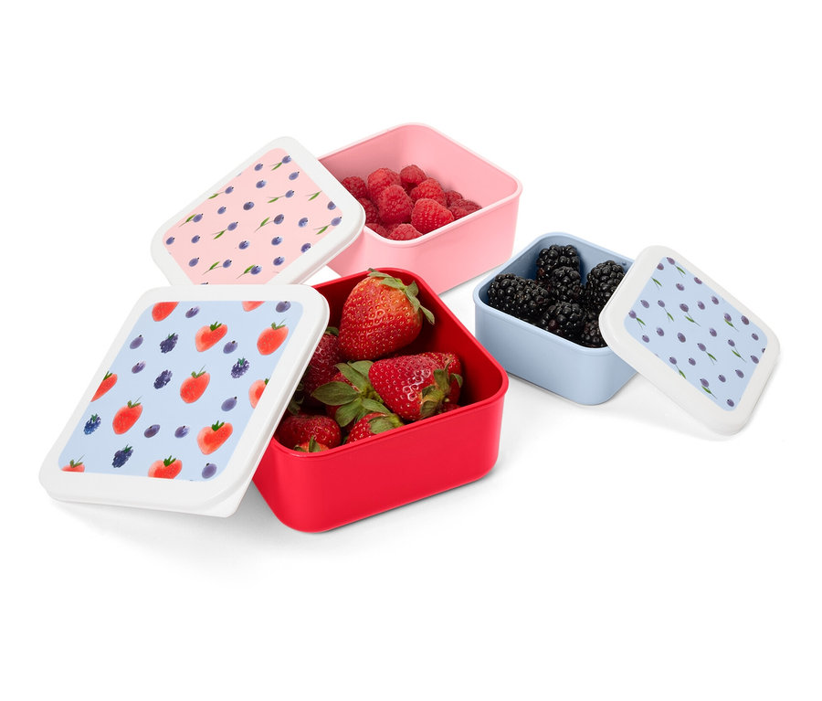 Quatre boîtes pour en-cas remplies de fruits. Une boîte rouge est remplie de fraises, une rose de framboises et une bleue de mûres.