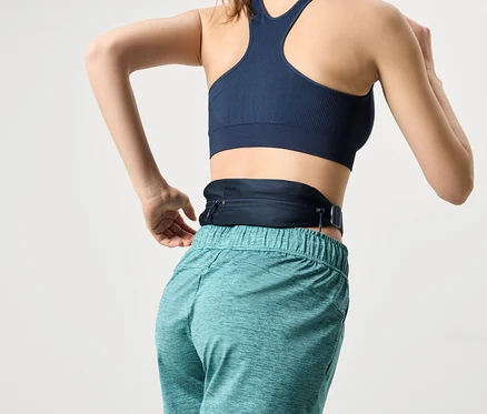Femme vue de dos portant un soutien-gorge de sport bleu marine et un short turquoise, avec une banane bleu marine autour de la taille.