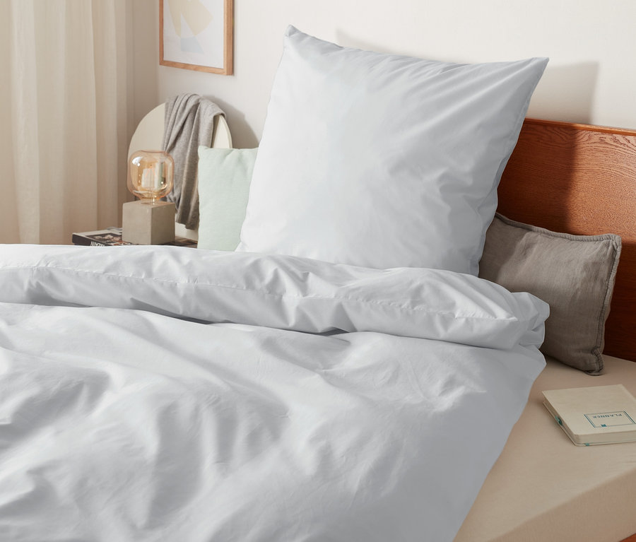 Gros plan sur une parure de lit en percale blanche de taille standard, grande taille et taille double sur un lit avec cadre en bois.