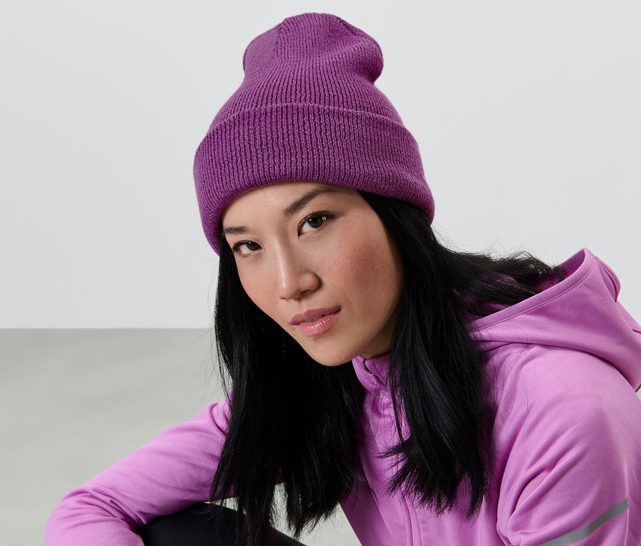 Une femme asiatique aux longs cheveux noirs porte un bonnet en maille violet et un sweat à capuche violet.