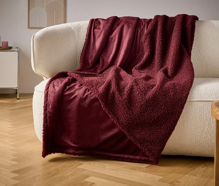 Une couverture bordeaux drapée sur un canapé crème.