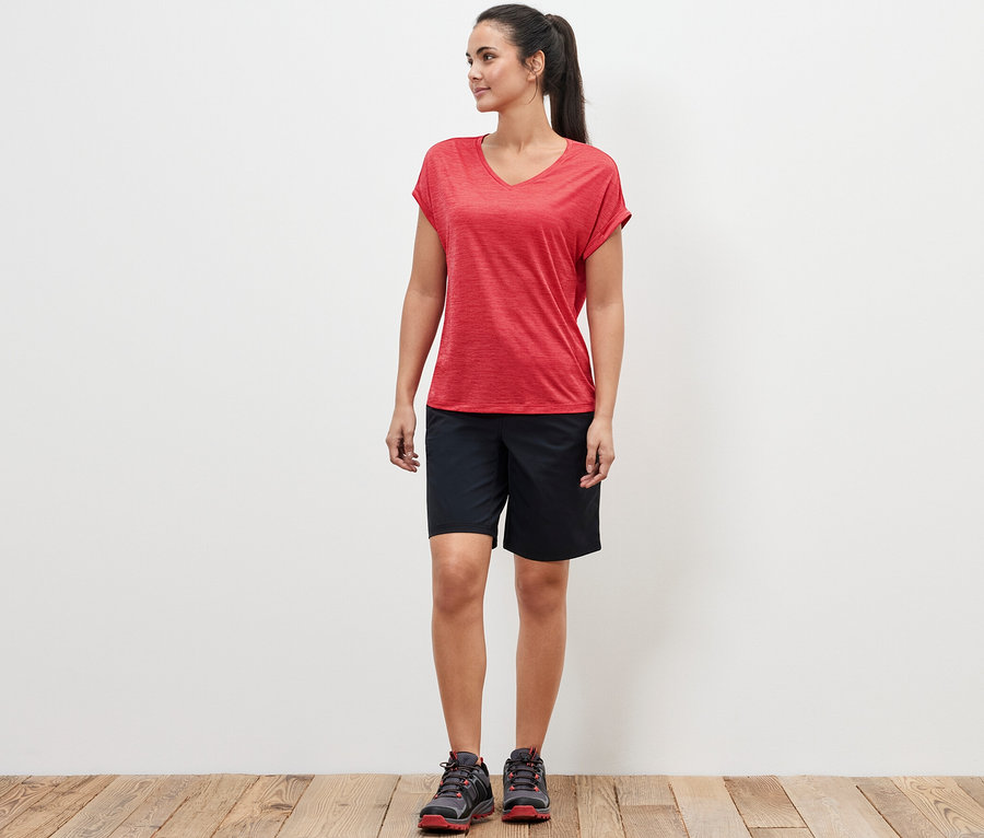 Une femme debout portant un t-shirt technique rose vif et un short noir.