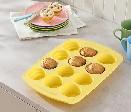 Moule à muffins jaune avec quelques muffins, assiettes avec des muffins et des verres sur un plan de travail.