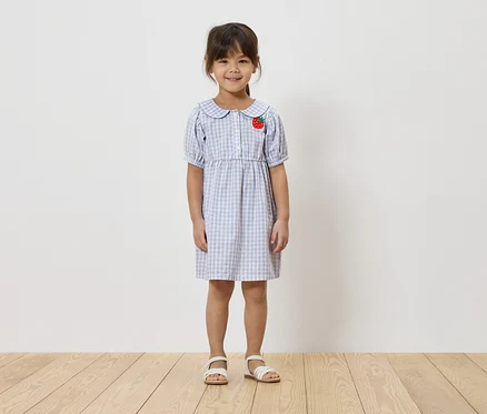 Fillette portant une robe à carreaux bleu clair avec une application fraise et des sandales blanches.
