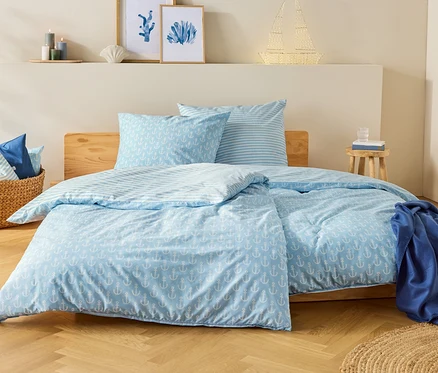 Un lit bleu et blanc à motif d'ancres dans une chambre. Un verre d'eau est posé sur la table de chevet.