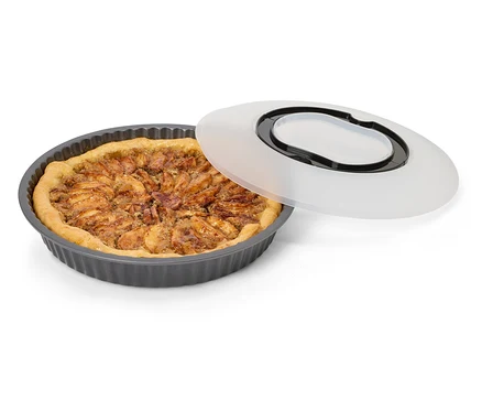 Un moule à tarte rond cannelé gris foncé avec une tarte aux pommes cuite et un couvercle translucide à poignée noire posé à côté.