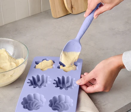 Une femme remplit de pâte un moule en silicone violet avec une cuillère à pâte multifonctions.