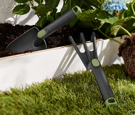 Une partie du kit d'outils de jardinage est posée sur l'herbe à côté d'une hortensia bleue.