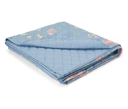 Une courtepointe bleu clair pliée avec un motif floral est posée sur un fond blanc.