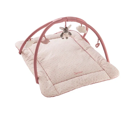 Tapis d'éveil rose pour bébé avec arche d'activités. Le tapis rose clair a de petits pois roses et une bordure rose foncé. De l'arche rose pendent un âne gris, deux nuages blancs, une baleine rose et un cœur rose.