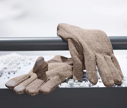 Des gants marron en matière polaire tricotée sont posés sur une surface enneigée.