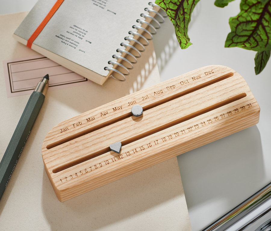 Un calendrier éternel en bois est posé sur une table à côté d'un bloc-notes et d'un stylo.