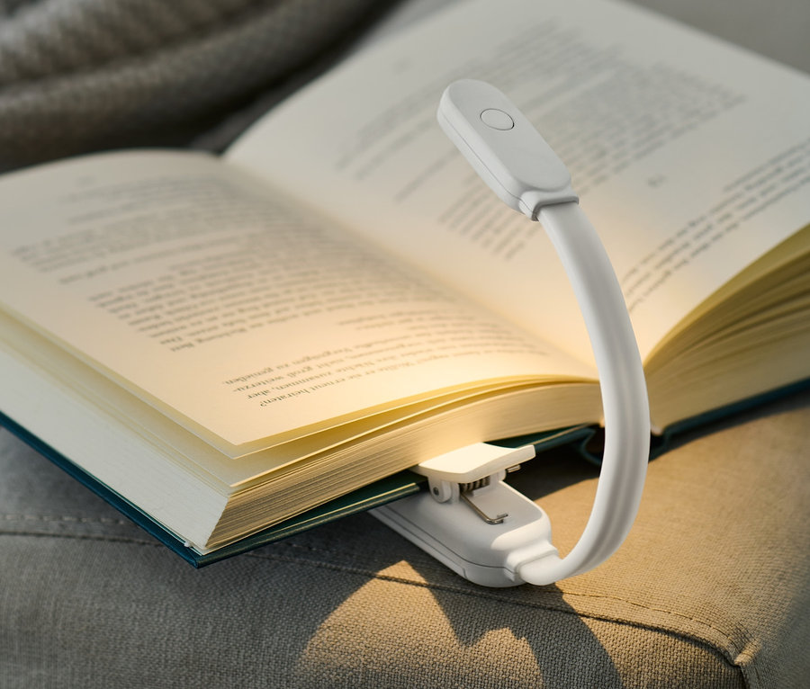 Livre ouvert avec une lampe de lecture LED posé sur un canapé gris.