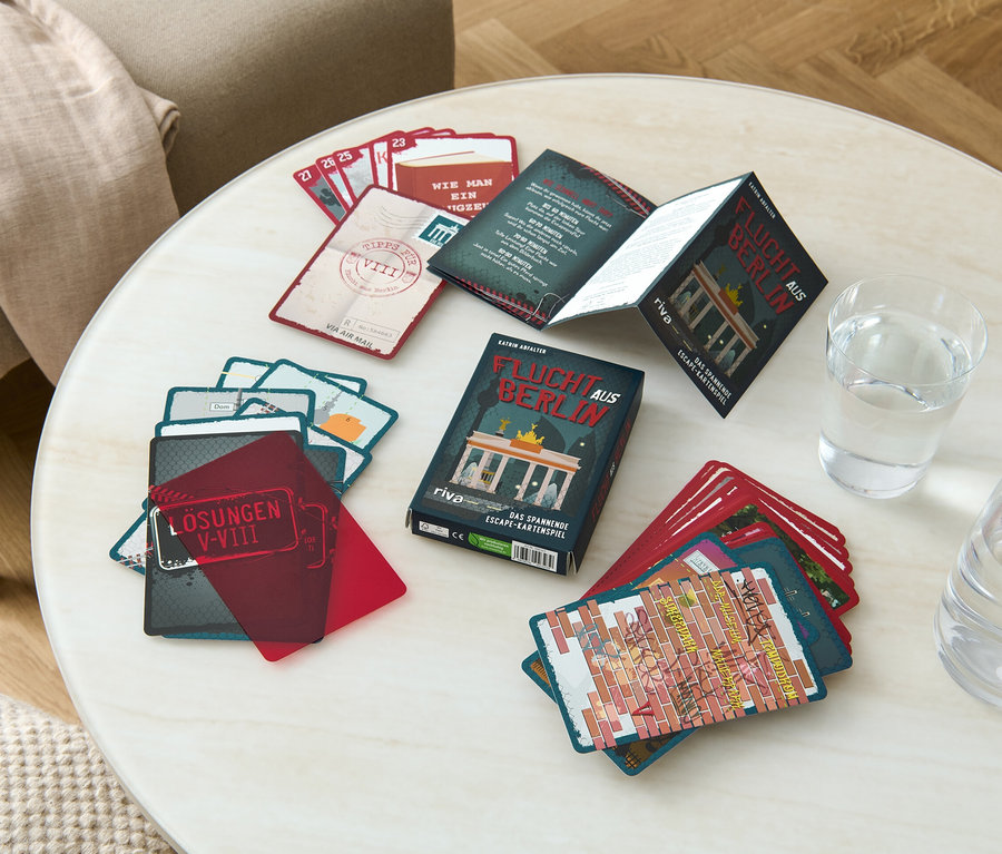 Sur une table se trouvent un jeu de cartes Escape Game « Flucht aus Berlin » (Sortir de Berlin, en allemand), un verre d'eau et une carafe.