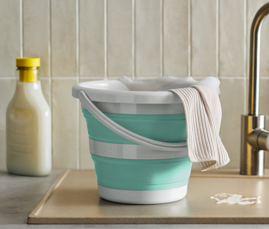 Un seau pliable avec un chiffon près d'un évier de cuisine.