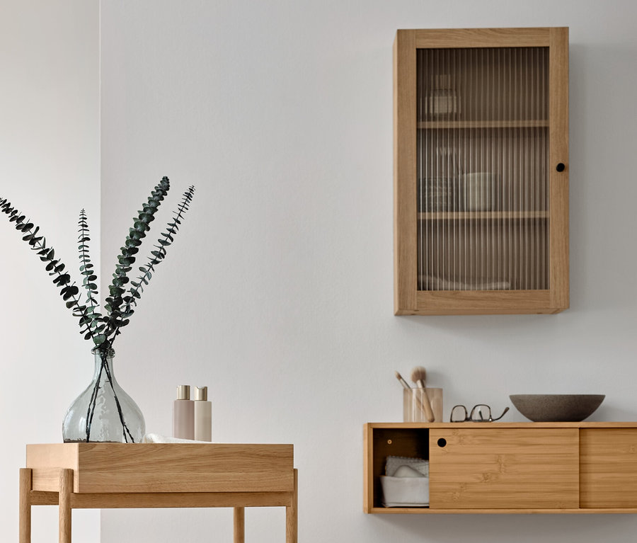 Aménagement d'une salle de bains avec étagère sur pieds à 3 compartiments en bois, armoire murale avec porte en verre strié et sèche-serviettes en bois massif.