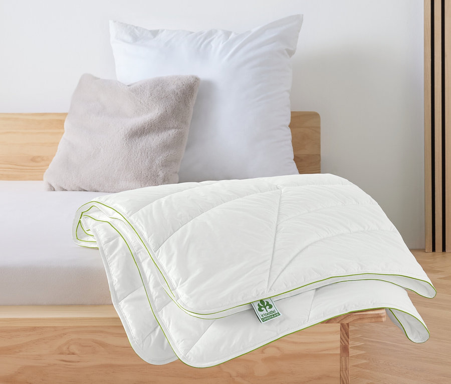 Une couverture matelassée blanche irisette® greenline avec technologie Outlast® est posée sur un lit.