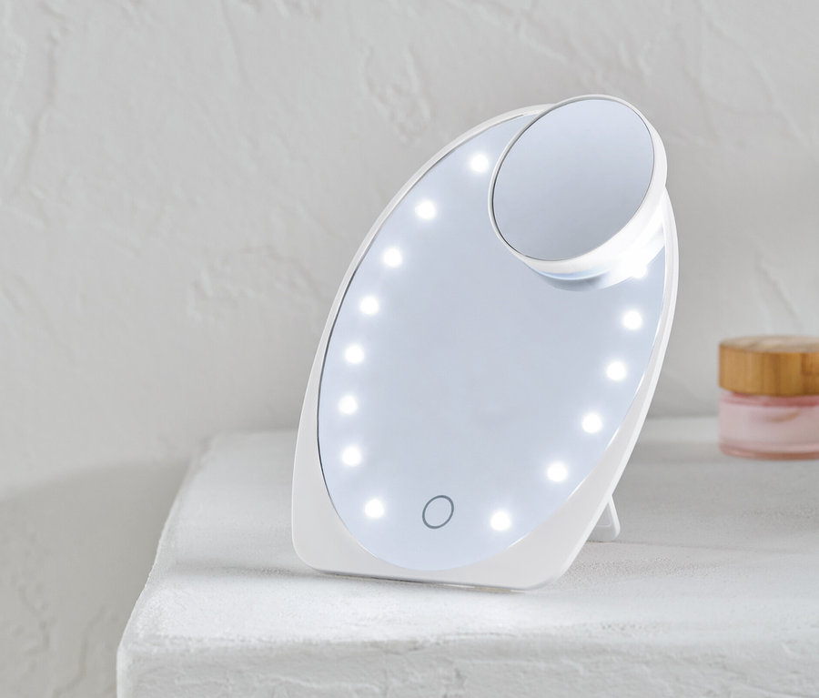 Un miroir cosmétique à LED éclairé est posé sur une surface blanche.
