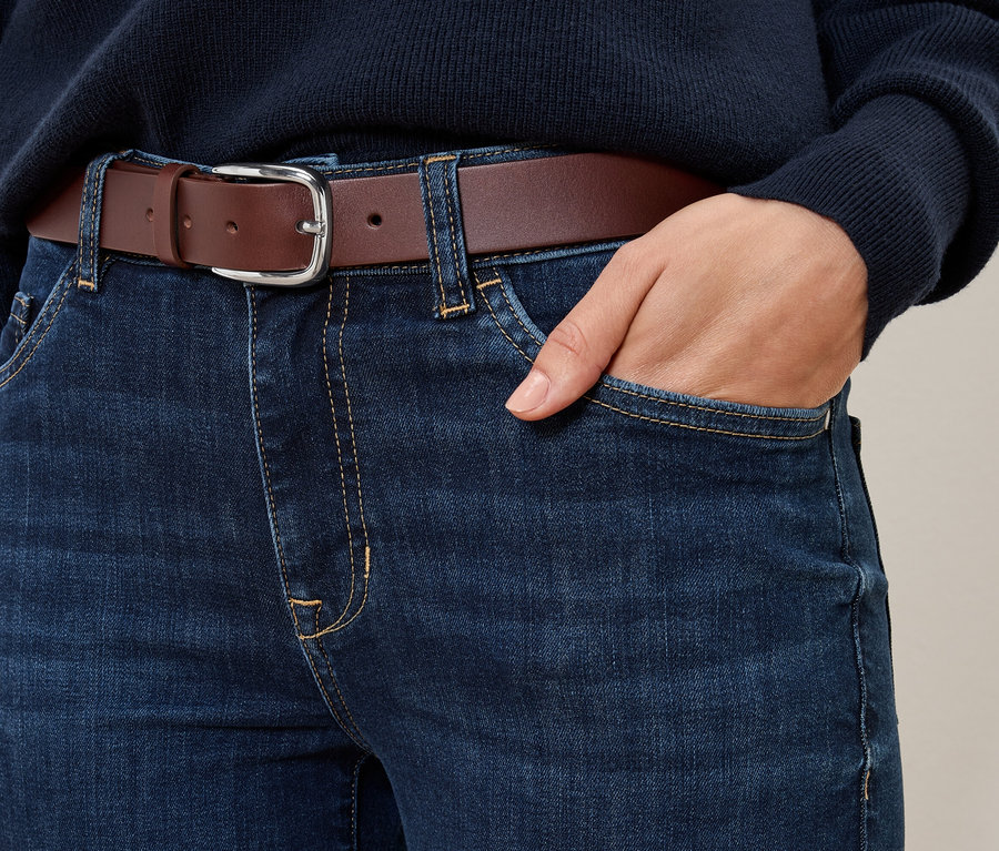 Gros plan sur un jean avec une ceinture en cuir cognac et une main dans la poche.