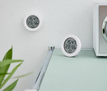 Deux horloges numériques blanches. Une horloge est sur le mur. La deuxième horloge est posée sur une table à côté d'une radio blanche.