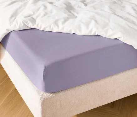 Gros plan d'un drap-housse violet sur un lit avec une couette blanche.
