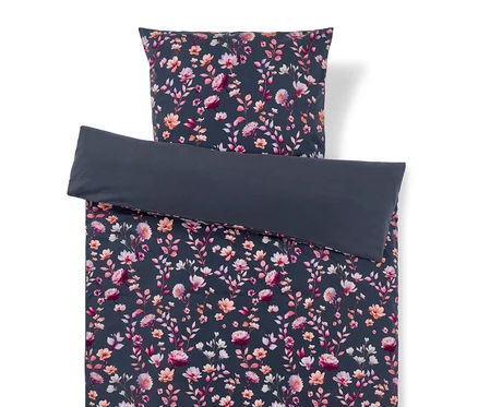 Parure de lit avec un motif floral rose, pêche et blanc sur fond bleu foncé/gris. La housse de couette est repliée, révélant un envers uni bleu foncé/gris, la taie d'oreiller est placée en haut.