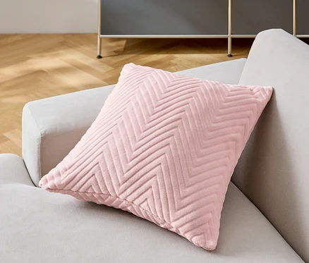 Un coussin décoratif rose à chevrons repose sur un canapé gris.