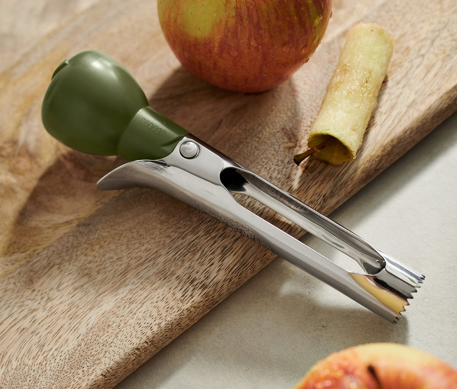 Un vide-pomme est posé sur une planche à découper en bois à côté de deux pommes, dont l'une a été évidée.