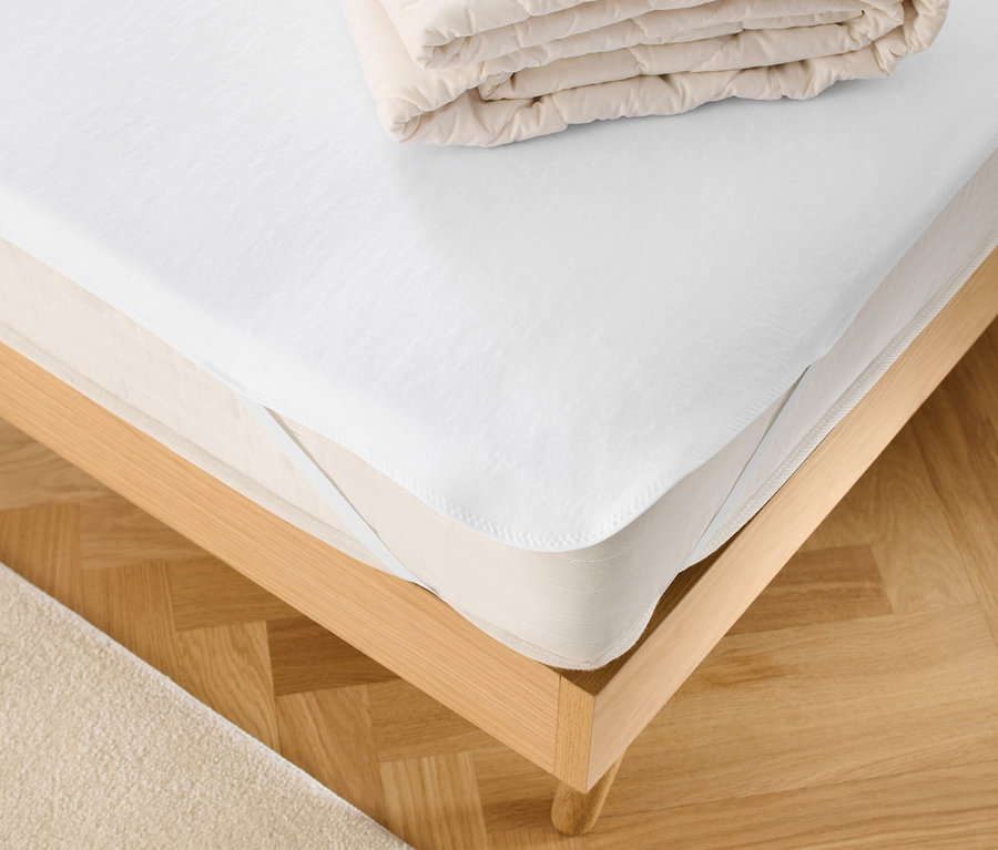 Sur un lit, un protège-matelas blanc et une couverture pliée.