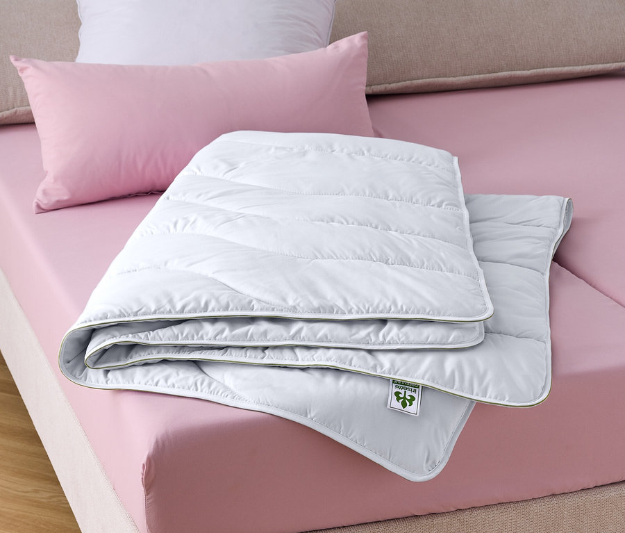 Une couette irisette® greenline Dacron® avec charbon actif est posée sur un lit.