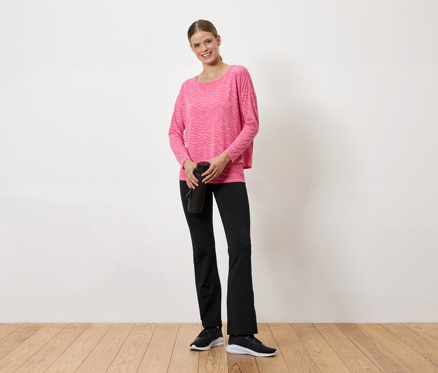 Femme en pull rose et pantalon noir tenant une bouteille d'eau noire.