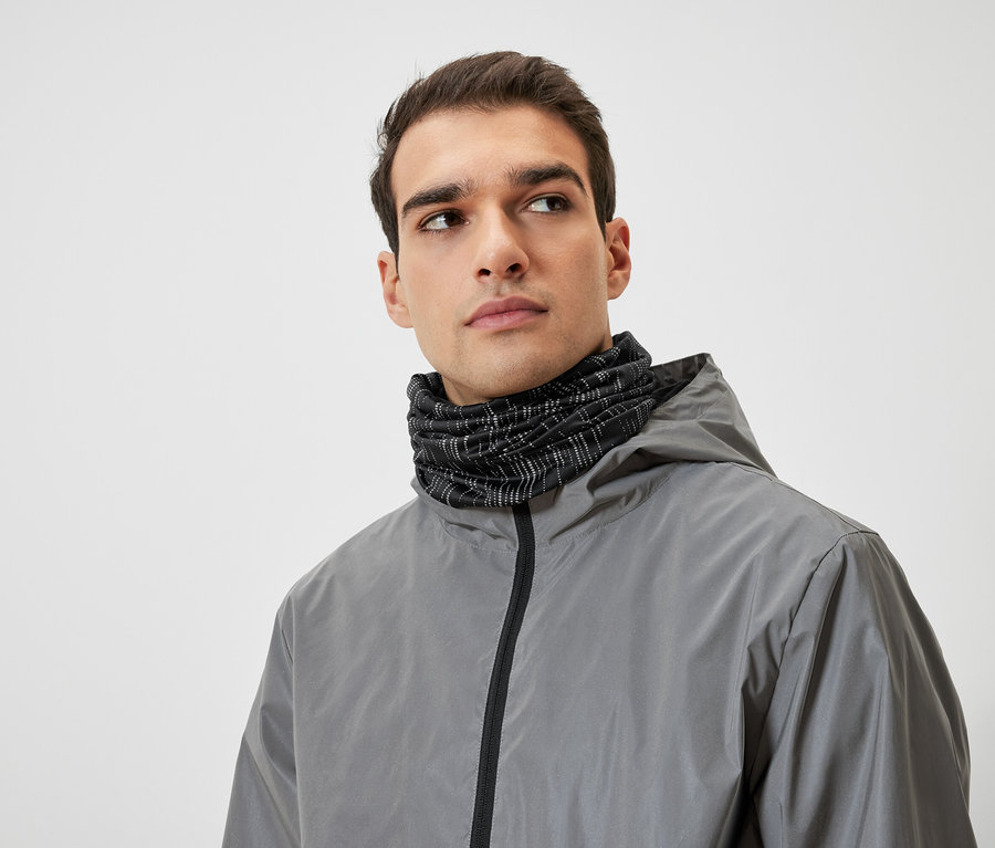 Un homme aux cheveux bruns porte une veste à capuche grise et un cache-cou noir.