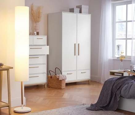 Dans la chambre, il y a un lampadaire avec abat-jour textile et une armoire de chambre « Eklund » avec tiroirs.