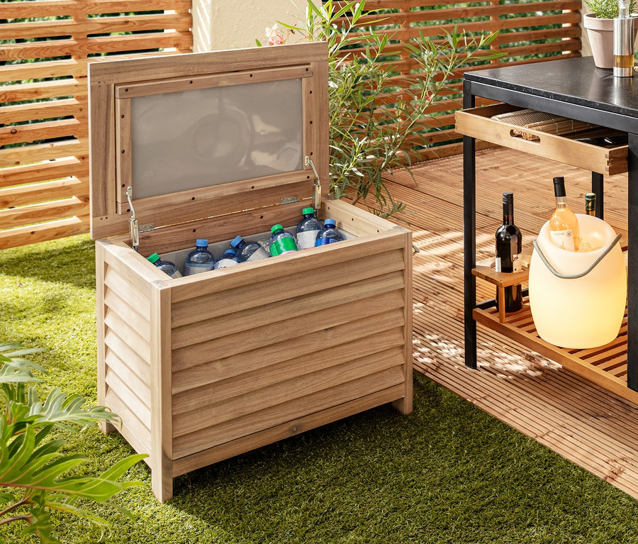 Sur la pelouse se trouvent une coolbox décorative avec ouvre-bouteille, à côté un chariot pour barbecue « Elin » avec tiroir, sur une table une lampe de table à LED sans fil et un rafraîchisseur de bouteilles à LED.