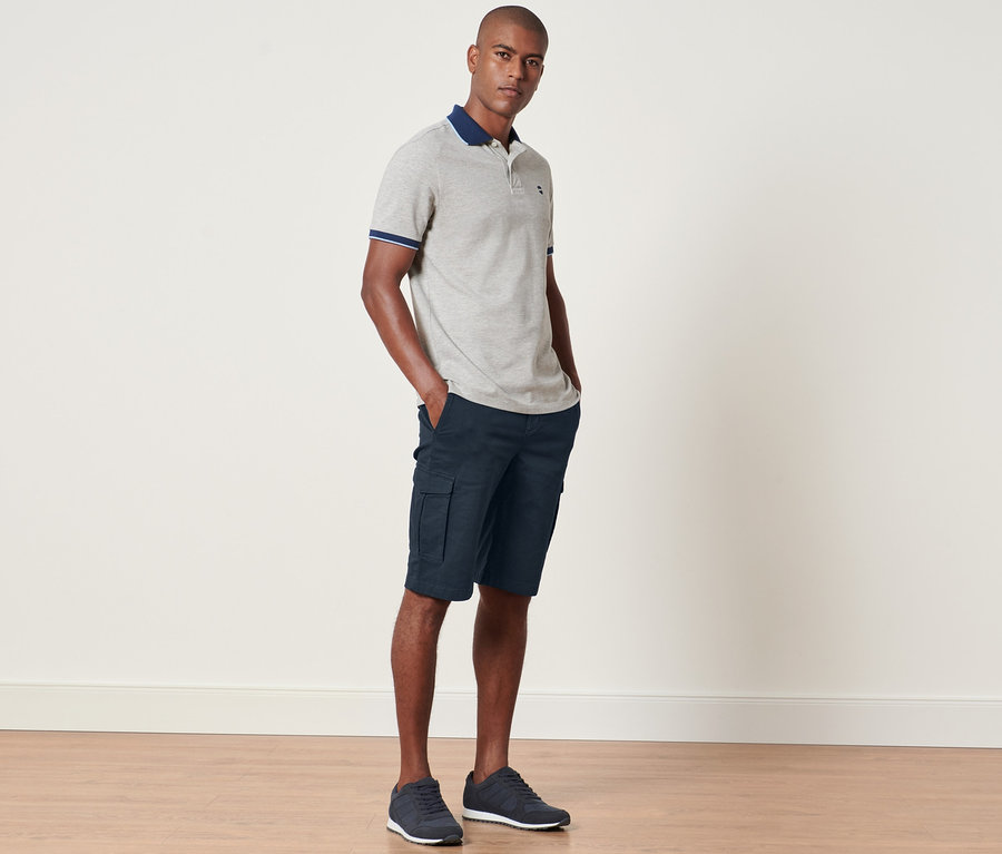 Un homme debout, les mains dans les poches d'un short cargo bleu marine.