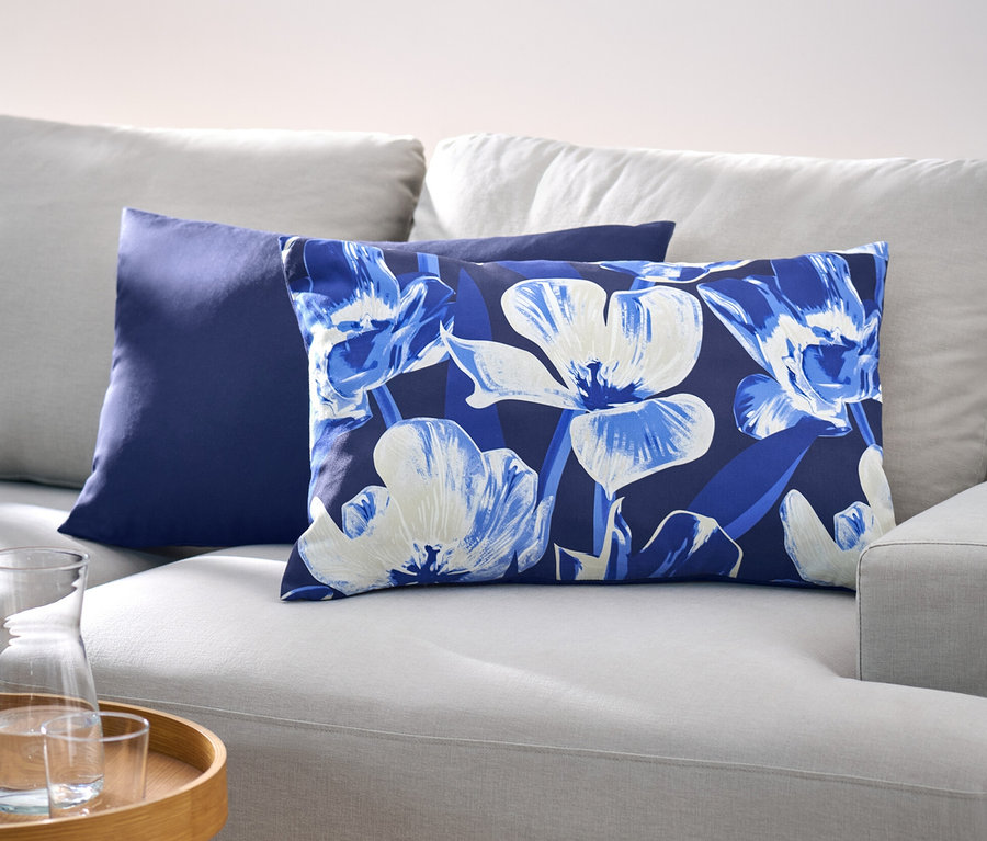 Sur un canapé gris clair se trouvent deux housses de coussin décoratif, l'une bleu foncé et l'autre à motif floral.