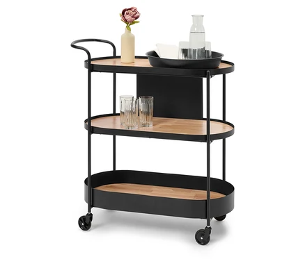 Un chariot de bar noir avec trois étagères en bois marron, sur l'étagère supérieure un vase avec une fleur, une carafe d'eau et des verres.
