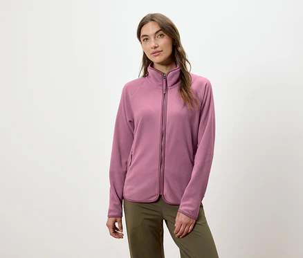 Une femme porte une veste en polaire rose zippée et un pantalon vert.