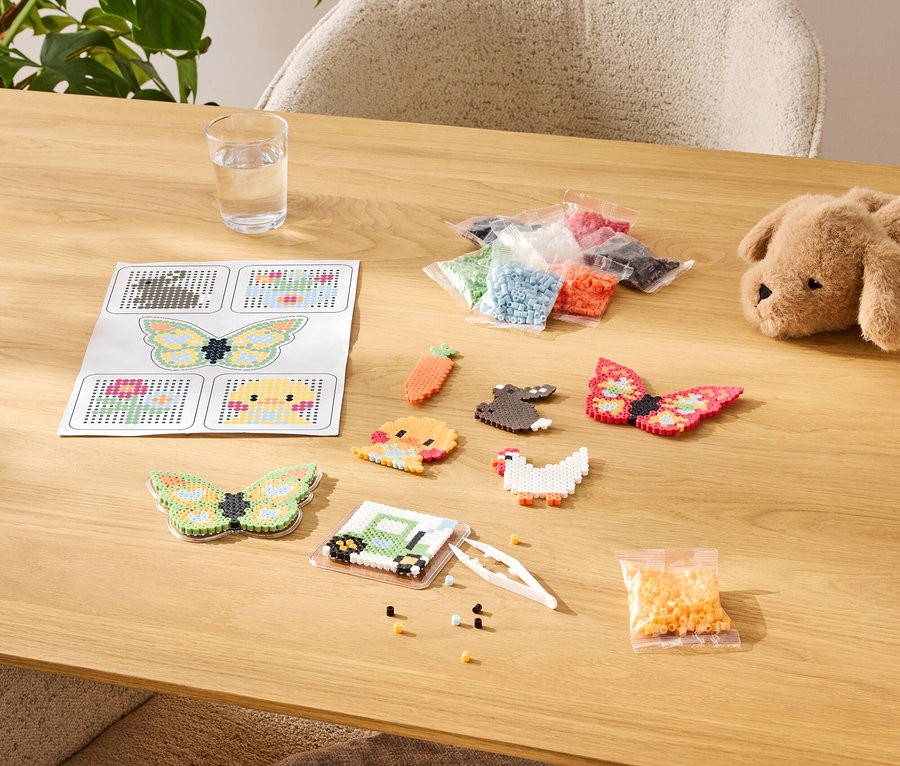 Table avec kit de bricolage de perles à repasser, comprenant des modèles, des motifs finis et des assortiments de couleurs en sachets.