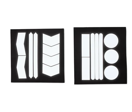 Deux feuilles noires avec des autocollants réfléchissants de différentes formes : bandes, flèches et cercles.