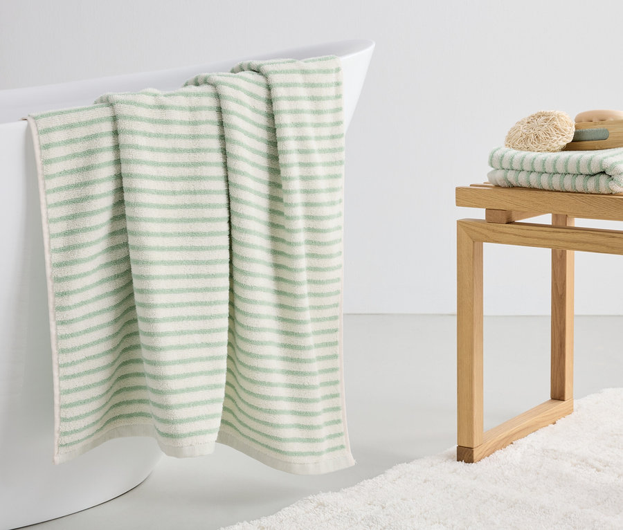 Une serviette de bain rayée verte est suspendue au bord d'une baignoire blanche.