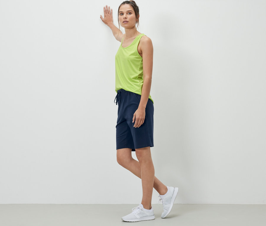 Une femme appuyée contre un mur porte un short en sweat bleu foncé.