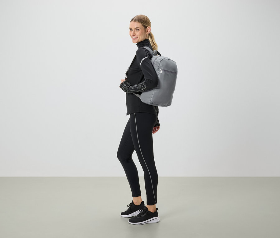 Femme en tenue de sport noire avec un sac à dos gris regardant par-dessus son épaule.